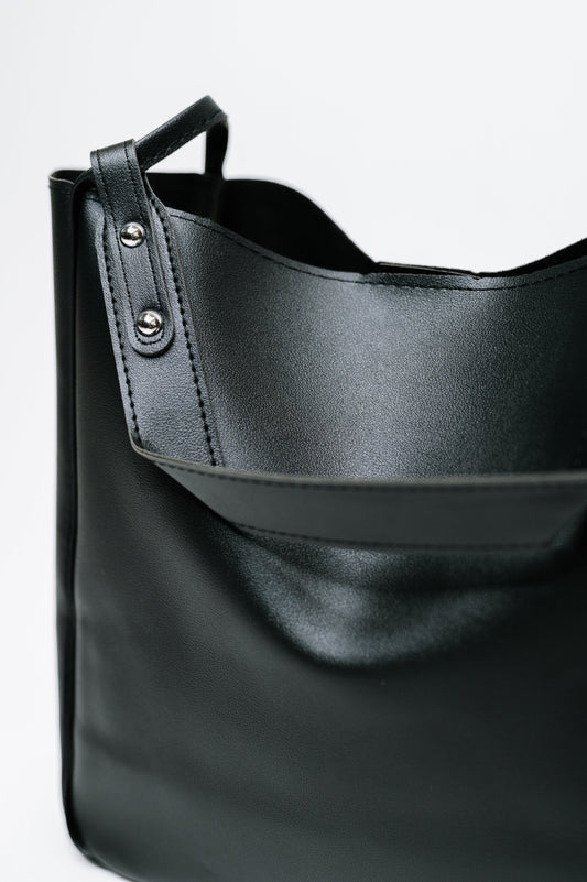 Black leather handbag with a strap on a light gray background