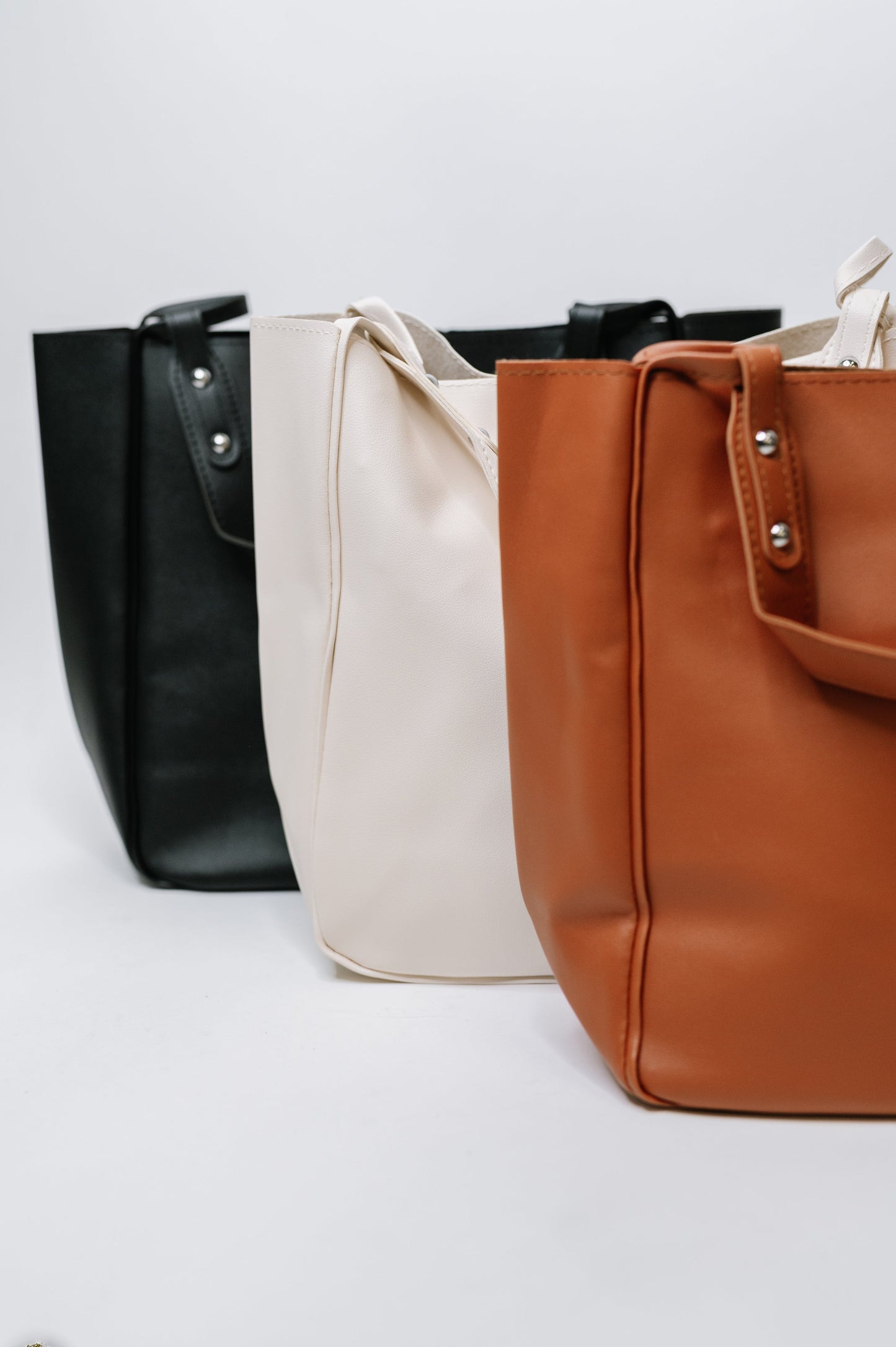 Three handbags in black, beige, and brown on a white background