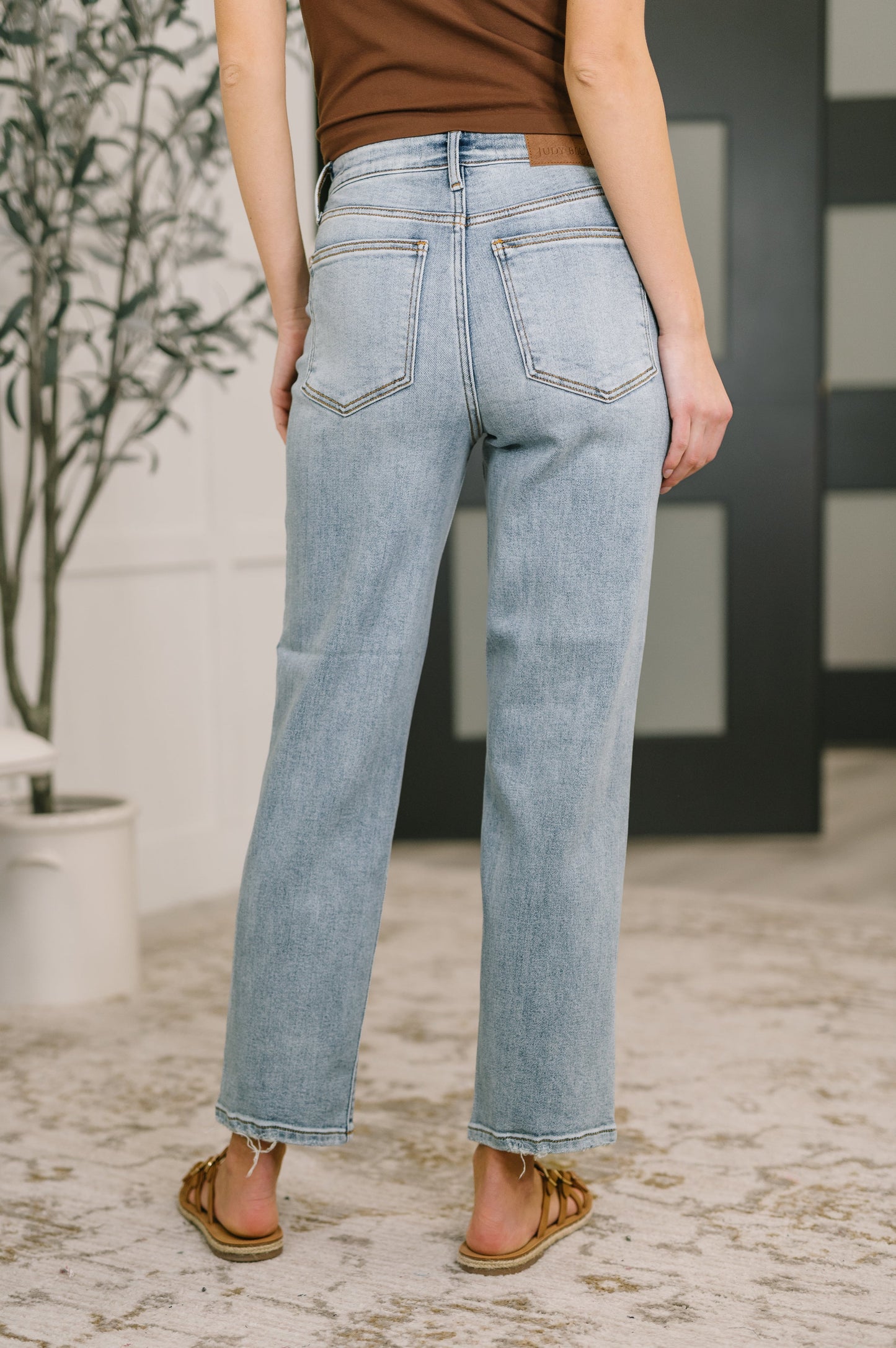Person wearing light blue jeans standing in a room with a plant and striped wall.