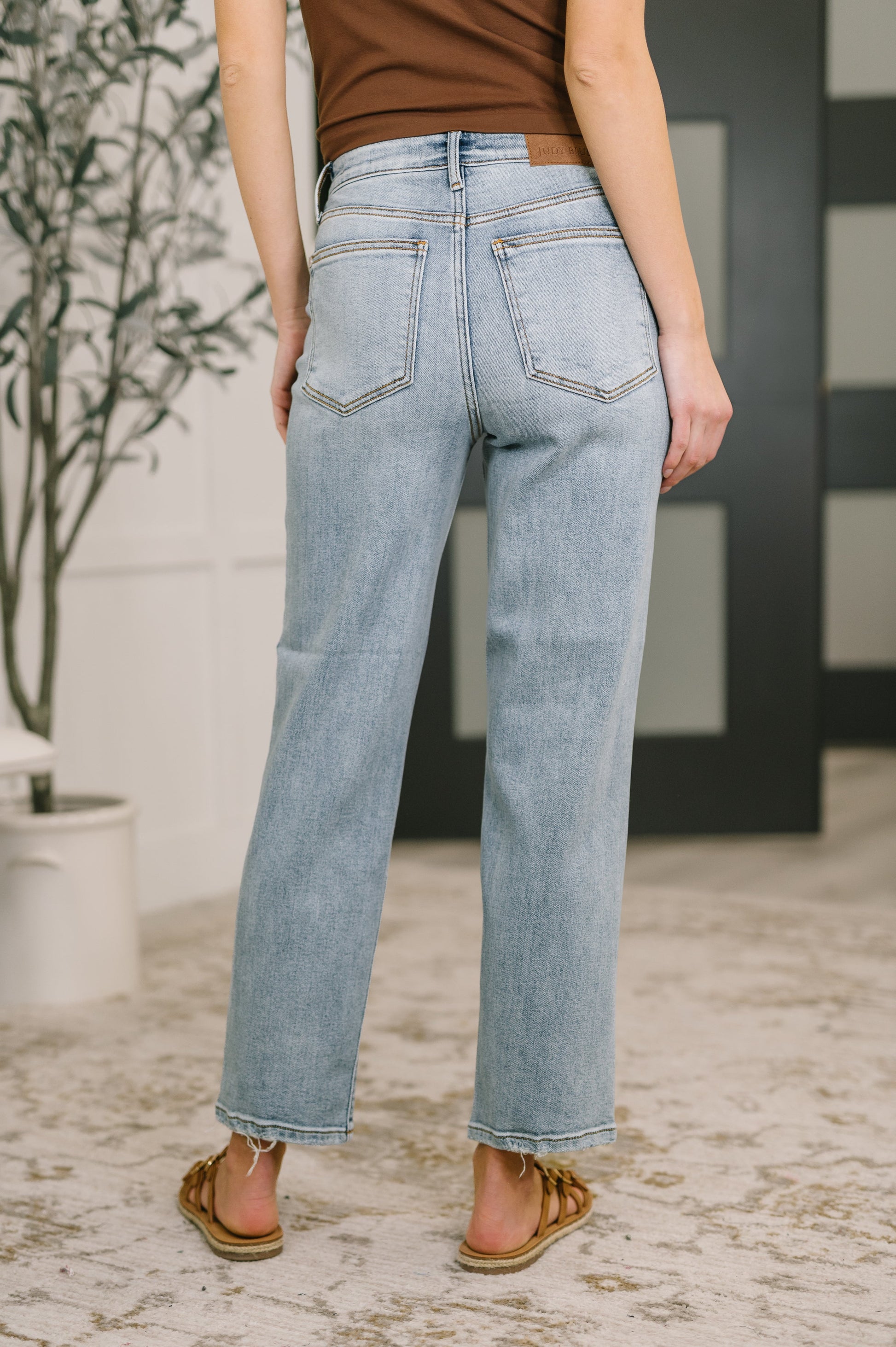 Person wearing light blue jeans standing in a room with a plant and striped wall.