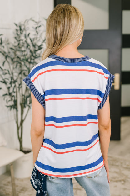 Woman wearing a striped shirt with blue, red, and white colors in an indoor setting.