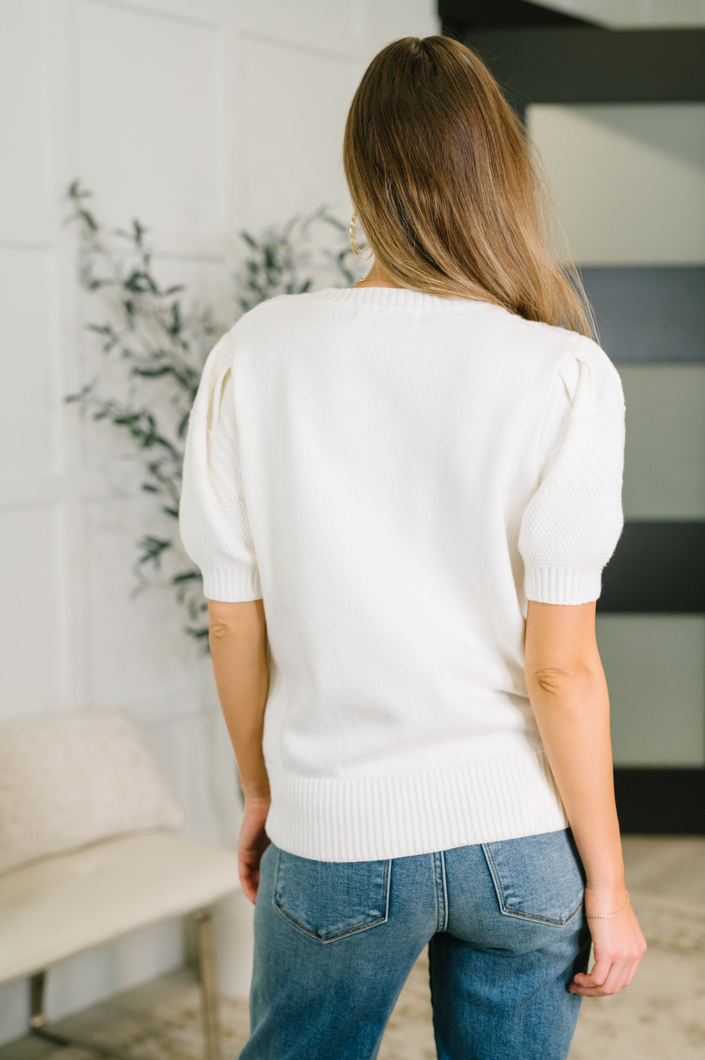 Woman wearing a white sweater and blue jeans in an indoor setting
