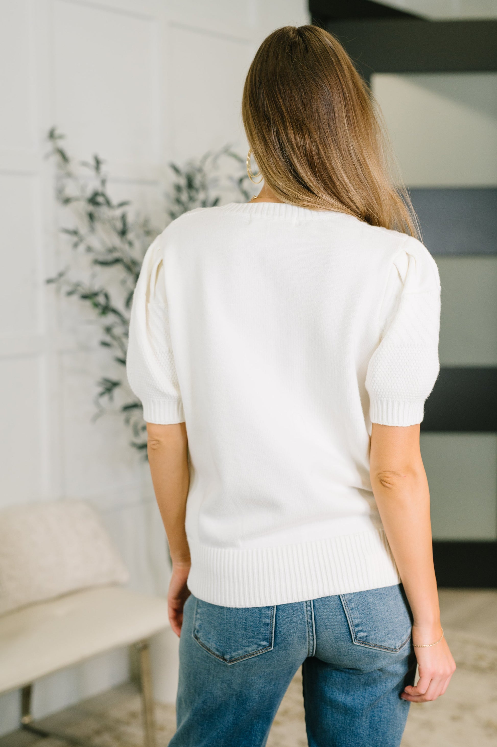 Woman wearing a white sweater and blue jeans in an indoor setting