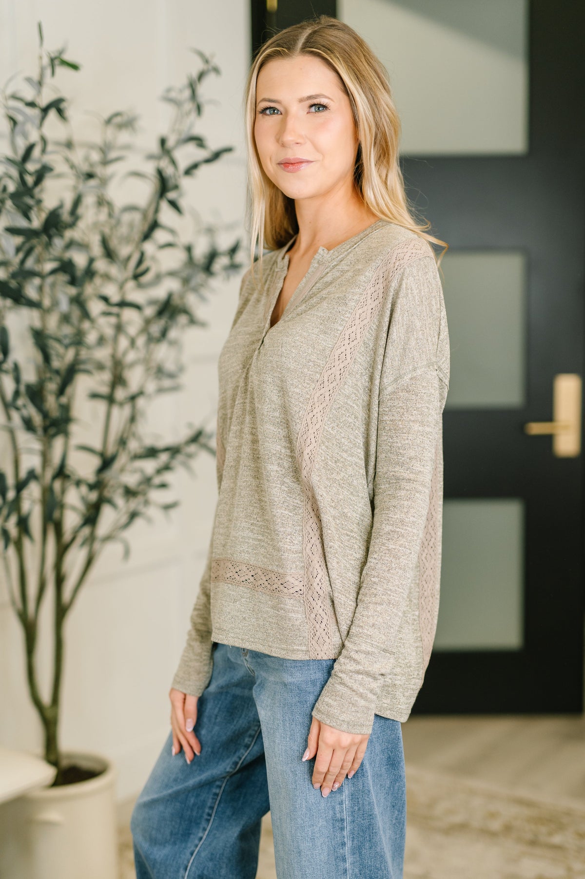 Woman wearing a beige sweater with lace details in an indoor setting.