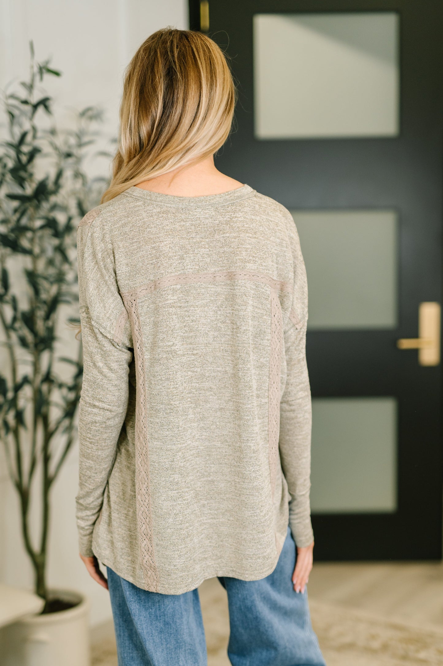 Person wearing a beige sweater and blue jeans standing in front of a black door.