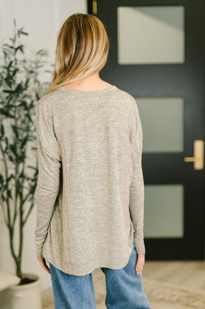 Person wearing a beige sweater and blue jeans standing in front of a black door.