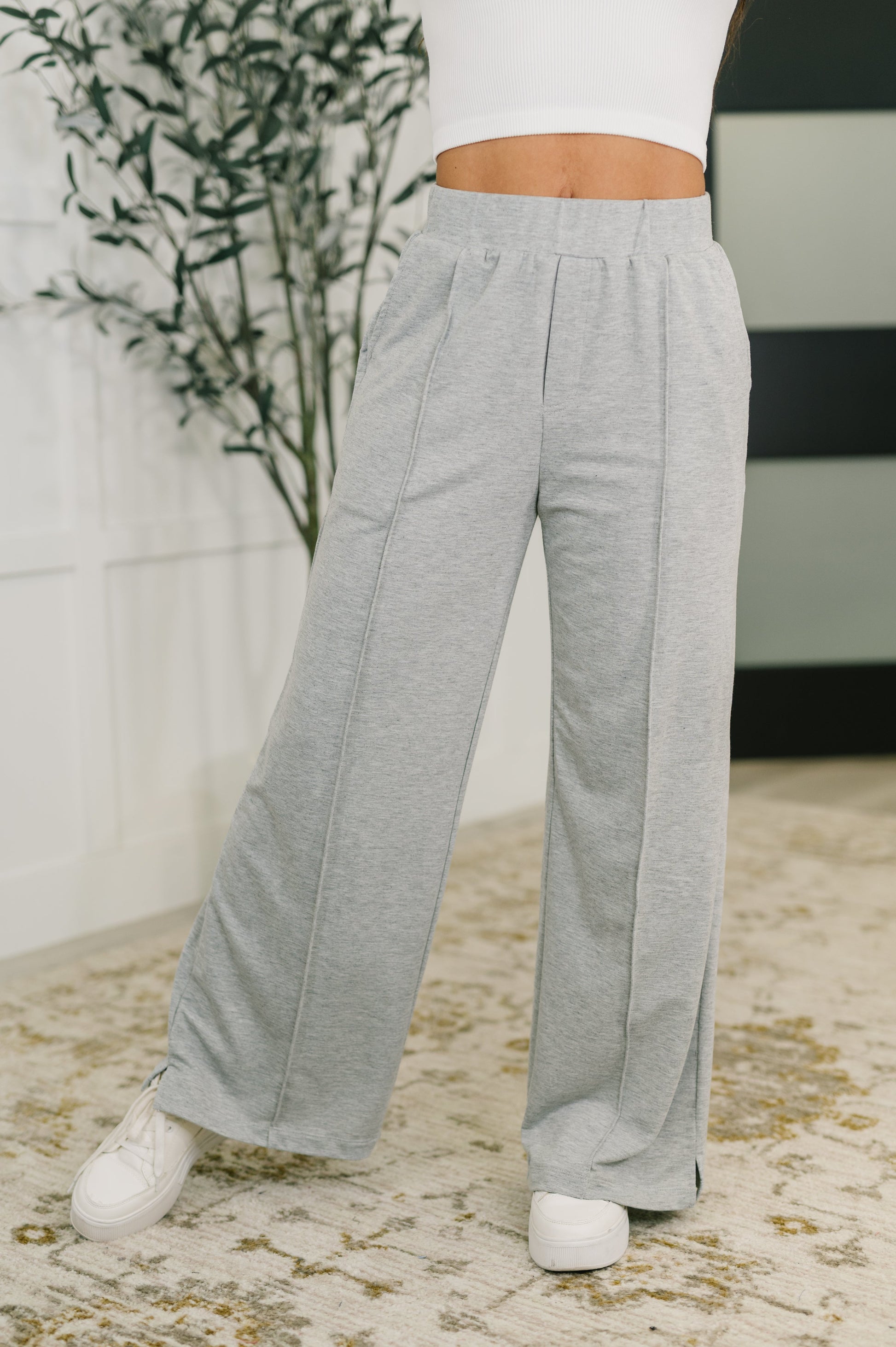 Person wearing gray wide-leg pants and white sneakers on a patterned rug.