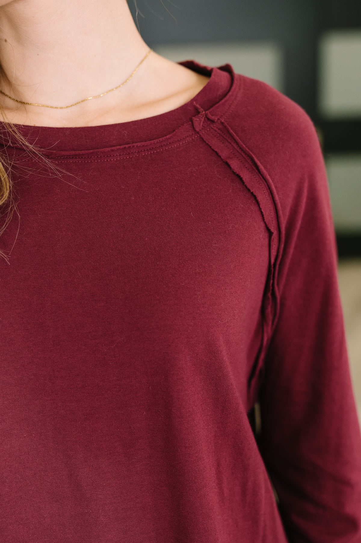 Close-up of a person wearing a long-sleeve raglan top in deep burgundy, showing the shoulder seam and neckline.