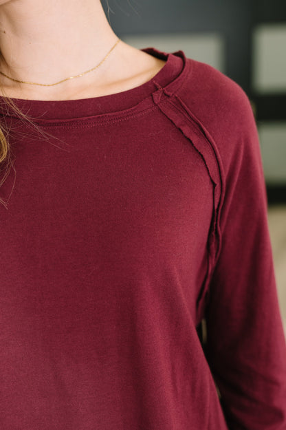 Close-up of a person wearing a long-sleeve raglan top in deep burgundy, showing the shoulder seam and neckline.