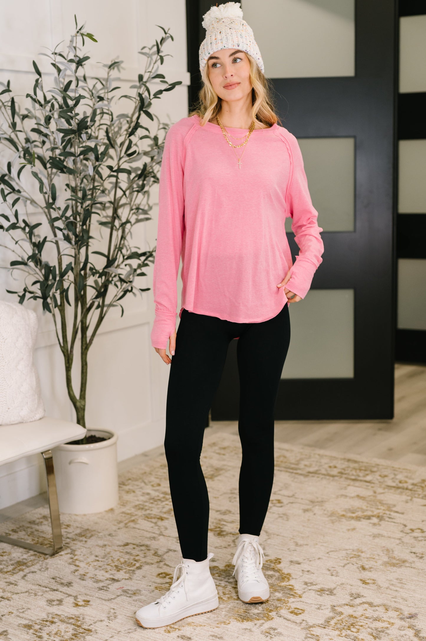 Woman wearing a pink long-sleeve top and black leggings standing indoors.