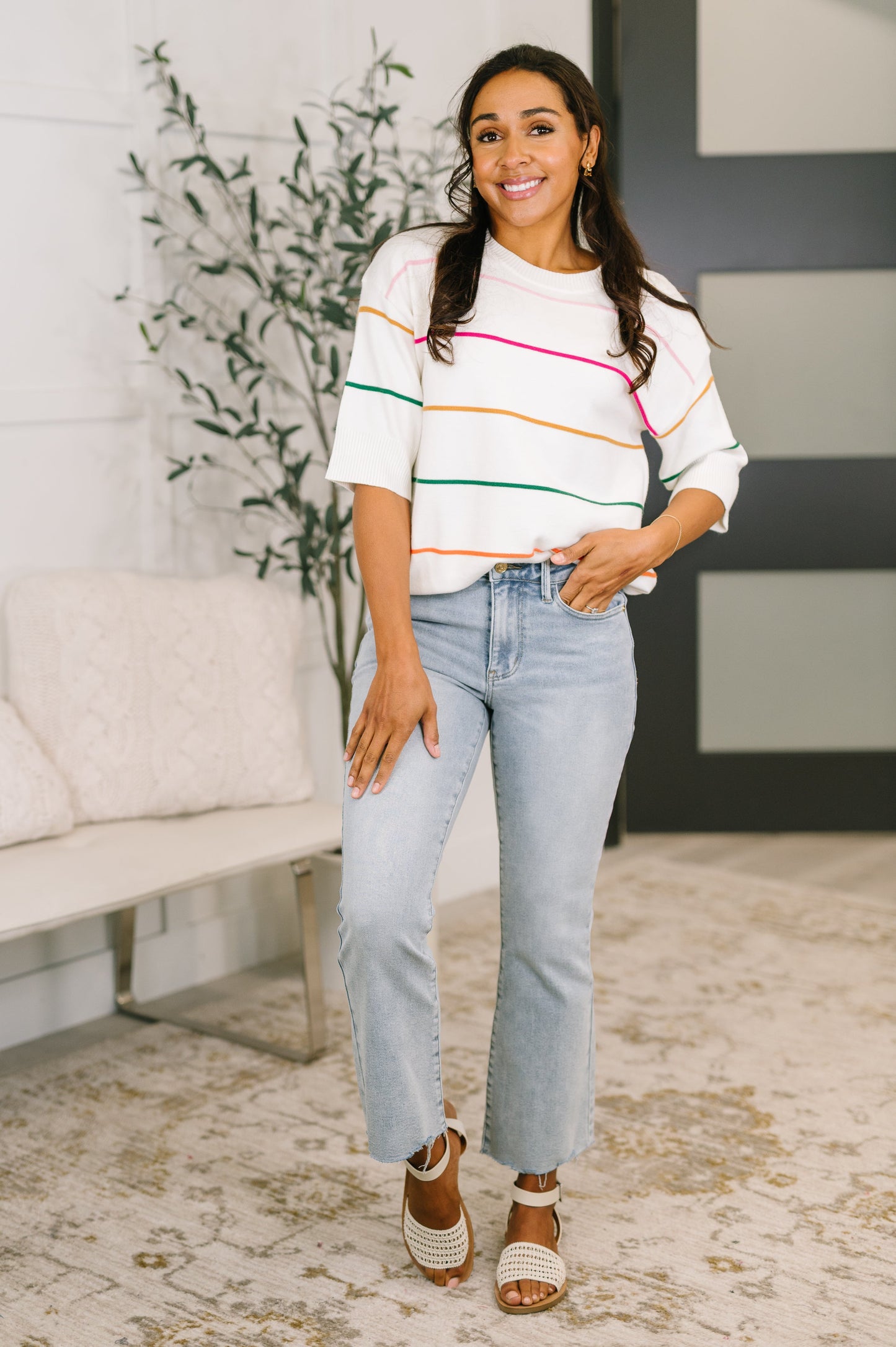 Woman wearing a colorful striped sweater and light blue jeans indoors.