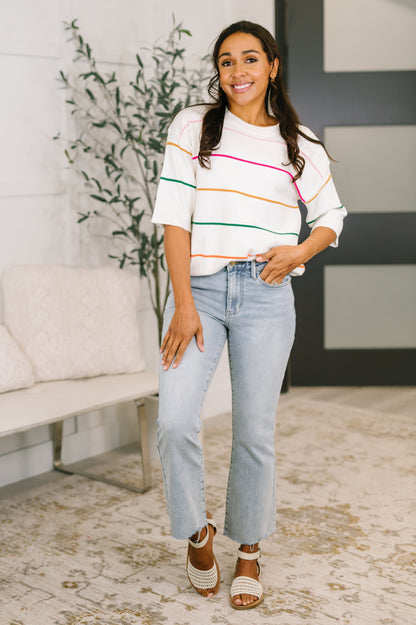 Woman wearing a colorful striped sweater and light blue jeans indoors.