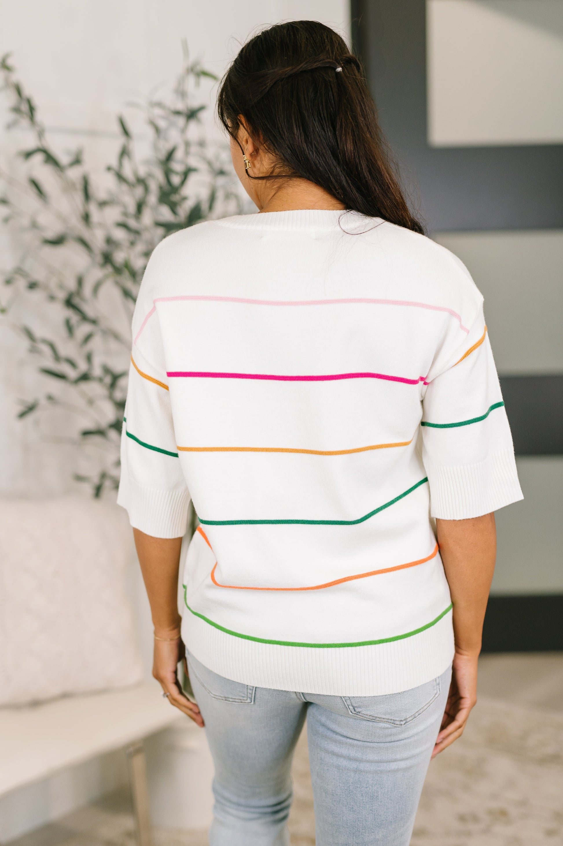 Woman wearing a white sweater with colorful stripes in an indoor setting