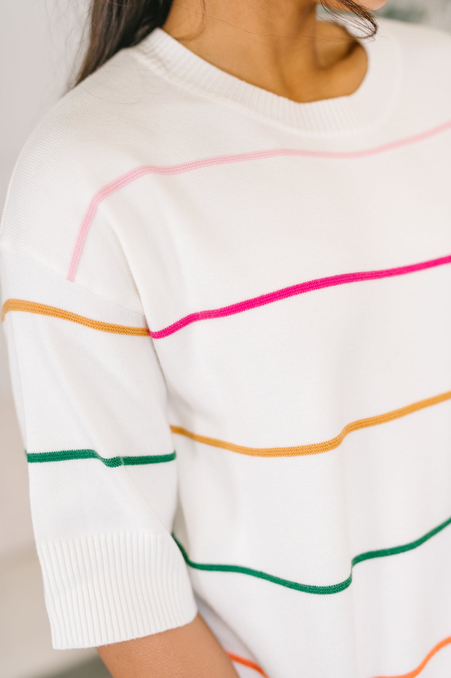 Close-up of a person wearing a white sweater with colorful stripes on a plain background