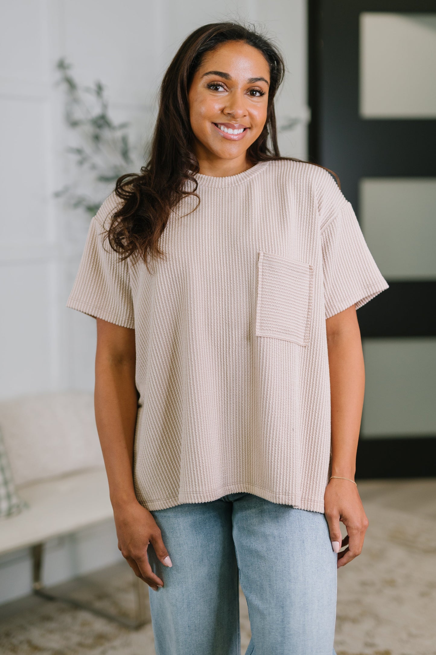 Woman wearing a beige ribbed t-shirt with a pocket in a casual setting.