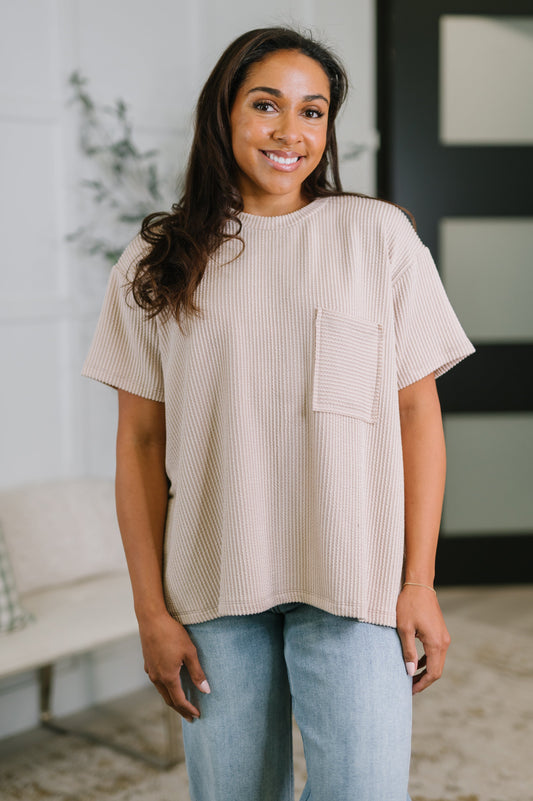 Woman wearing a beige ribbed t-shirt with a pocket in a casual setting.