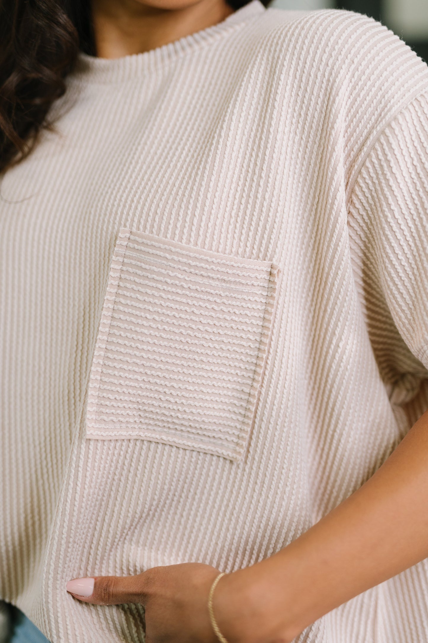 Close-up of a person wearing a beige textured sweater with a pocket.