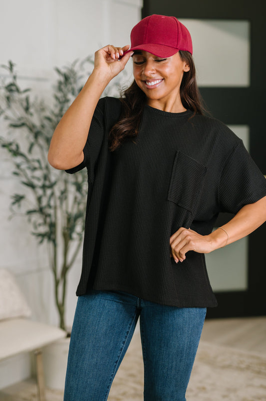 Woman wearing a black t-shirt, blue jeans, and a red cap indoors.