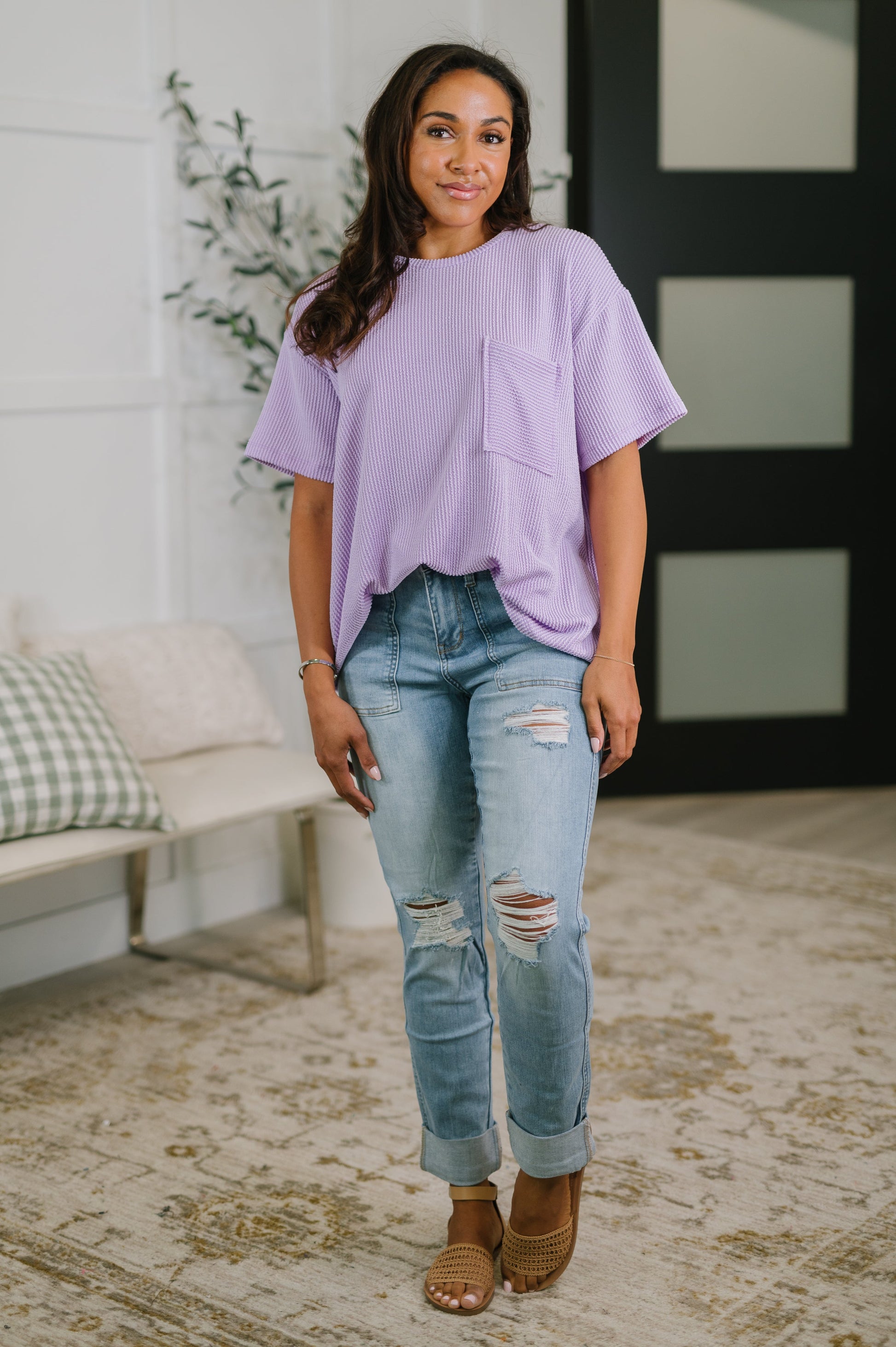 Woman wearing a light purple top and ripped jeans standing in a living room.