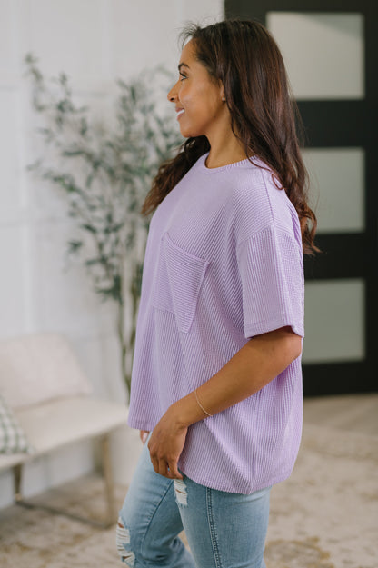 Woman wearing a light purple oversized shirt and blue jeans in an indoor setting.