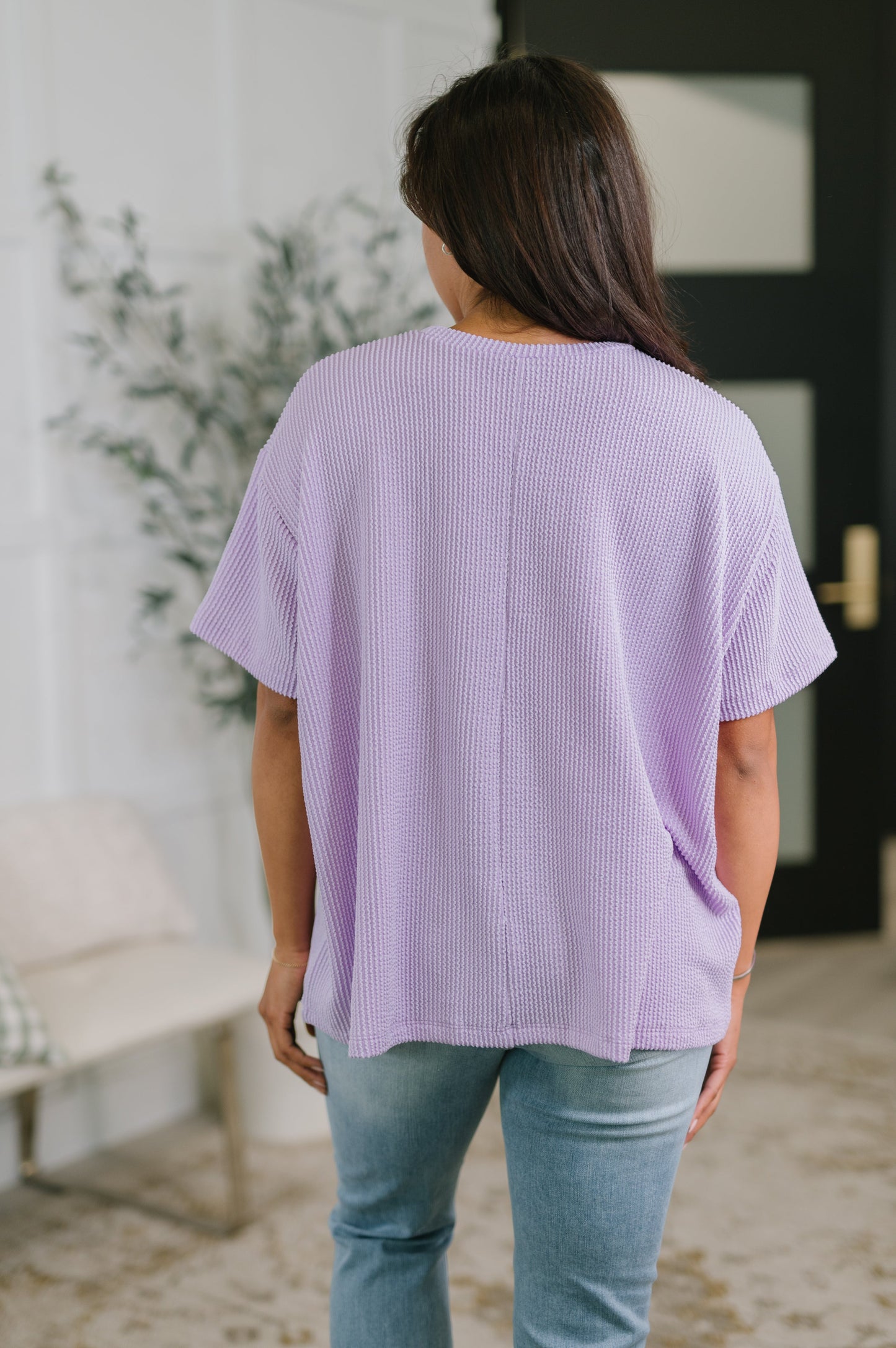 Person wearing a light purple ribbed sweater and blue jeans in an indoor setting.