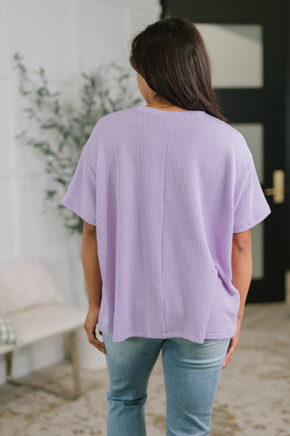 Person wearing a light purple ribbed sweater and blue jeans in an indoor setting.