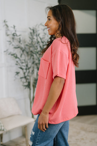 Woman wearing a pink blouse and blue jeans standing indoors with a plant in the background
