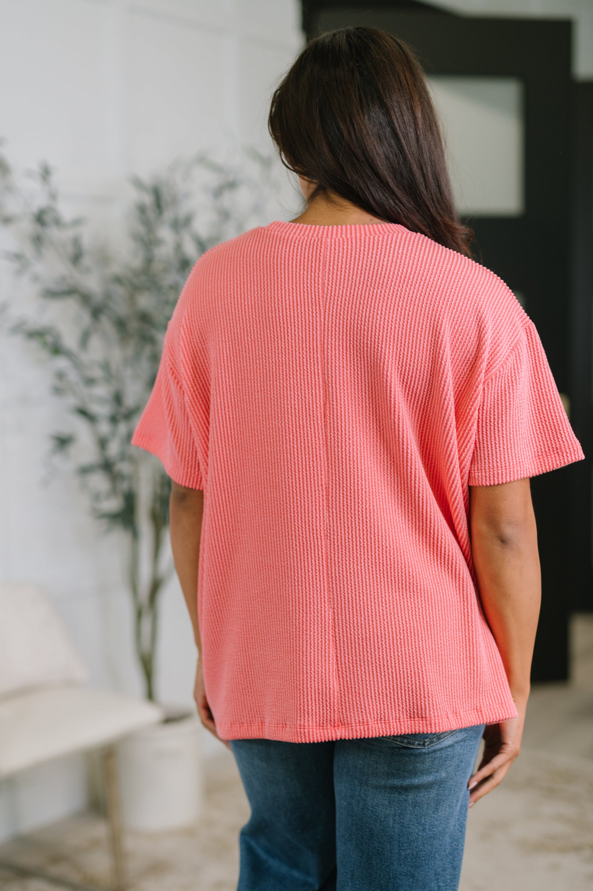 Person wearing a pink textured top and blue jeans in an indoor setting