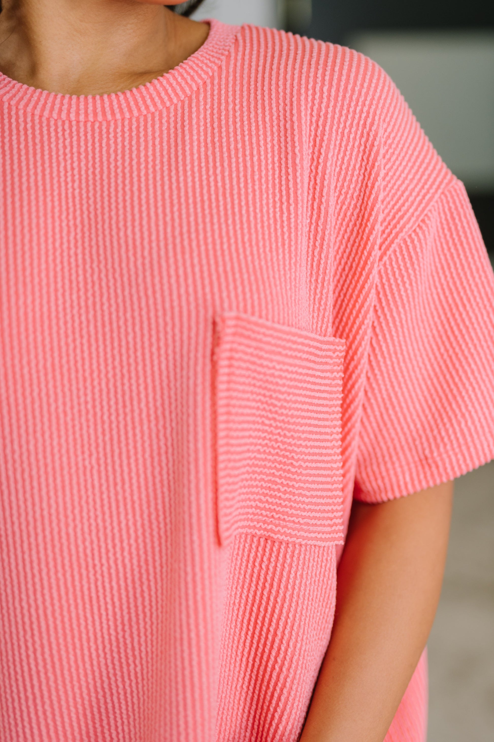 Close-up of a person wearing a pink textured dress with a pocket.