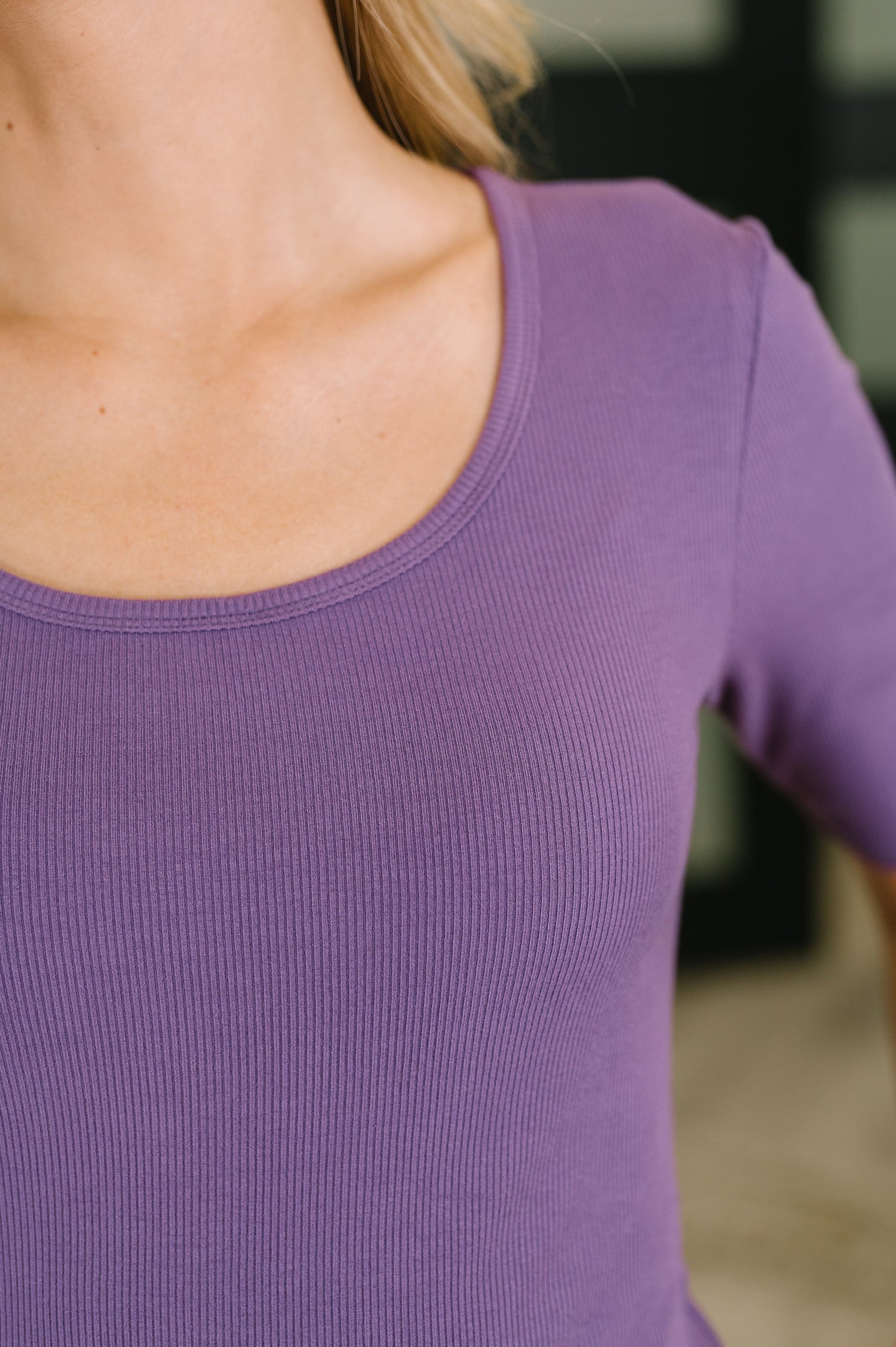 Close-up of a person wearing a short-sleeve ribbed scoop-neck top in a muted purple color.