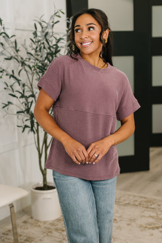 Woman wearing a maroon striped top and light blue jeans indoors.