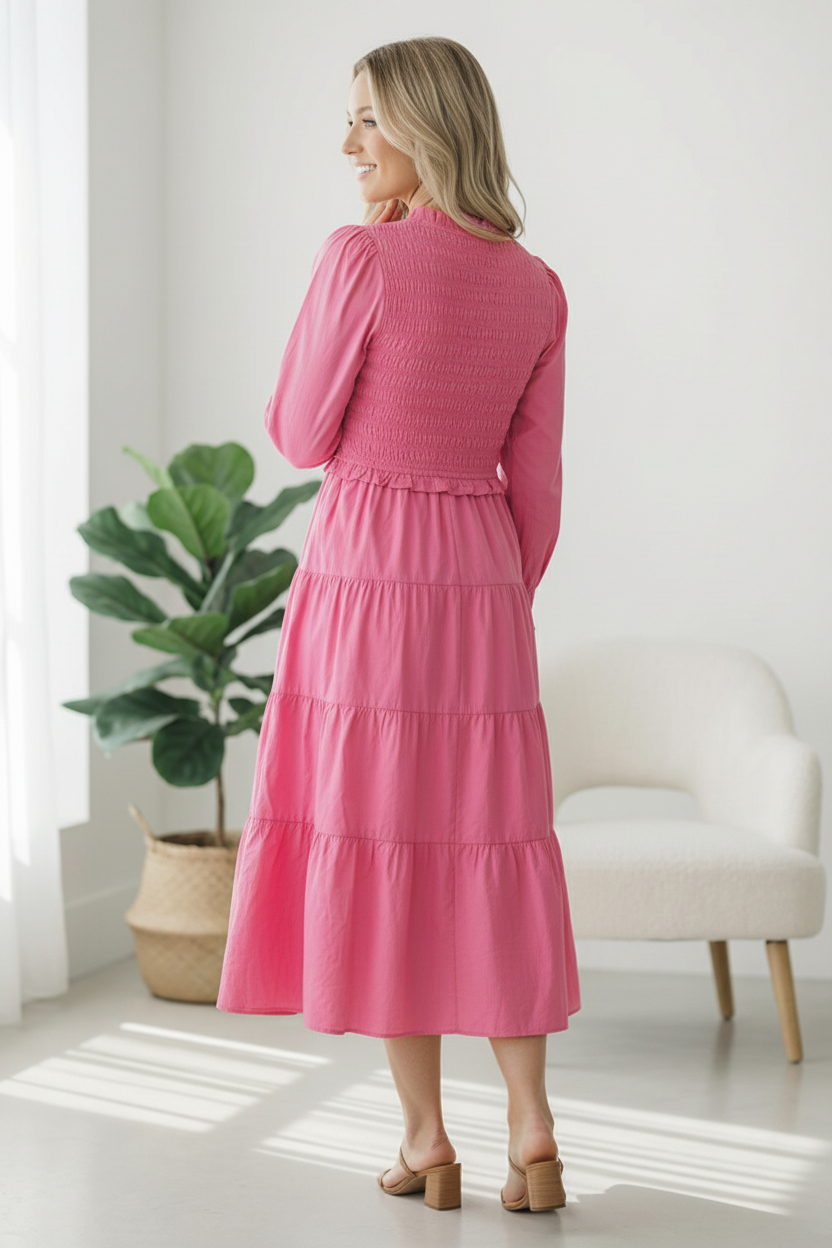 Woman wearing a pink dress standing in a bright room with a plant and chair.