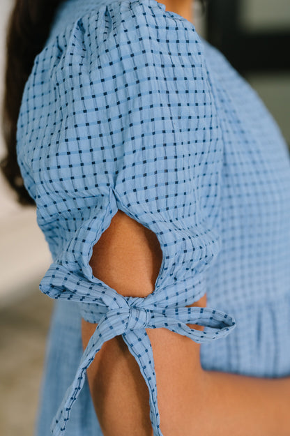 Close-up of a blue checkered blouse with tied sleeves.