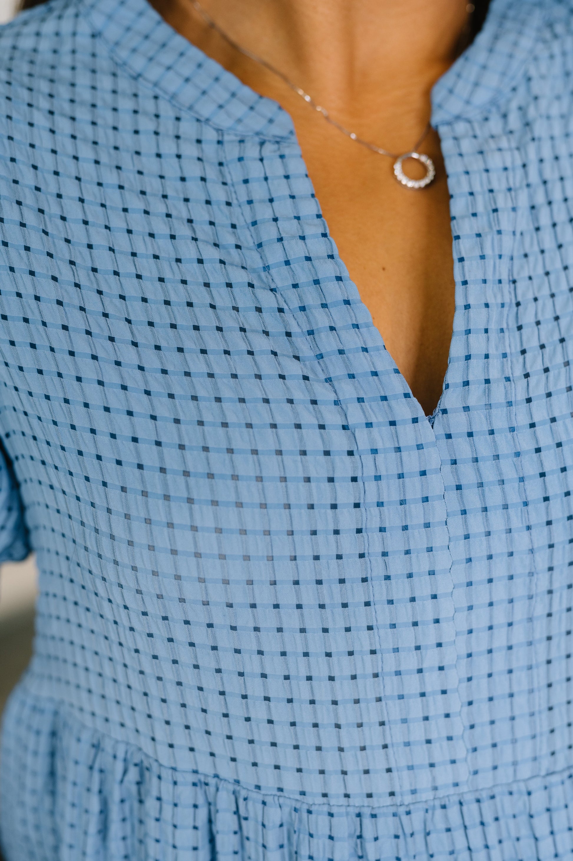 Close-up of a person wearing a blue checkered dress with a necklace.