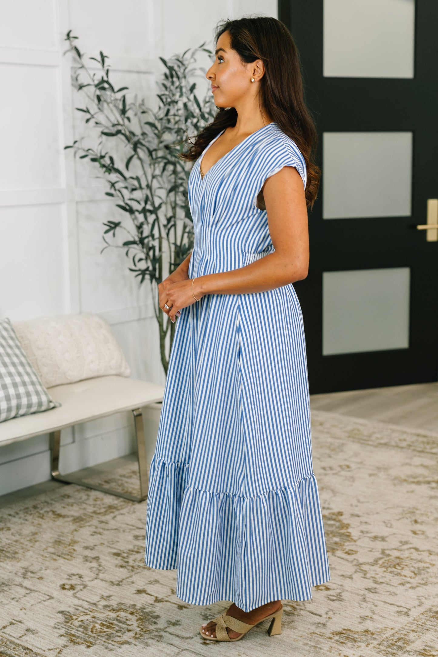 Woman wearing a blue and white striped dress in a room with a plant and bench.