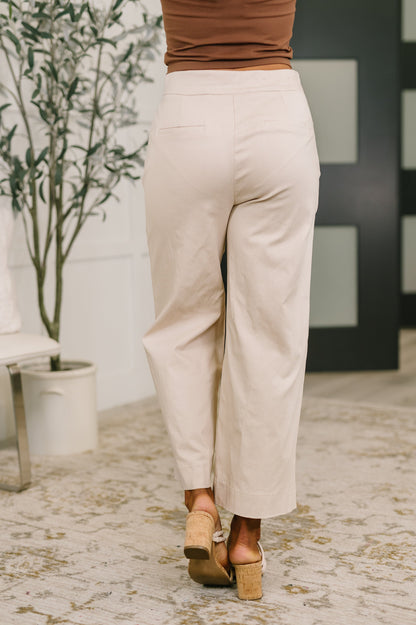 Person wearing beige pants and brown shoes in a room with a plant and decorative wall.