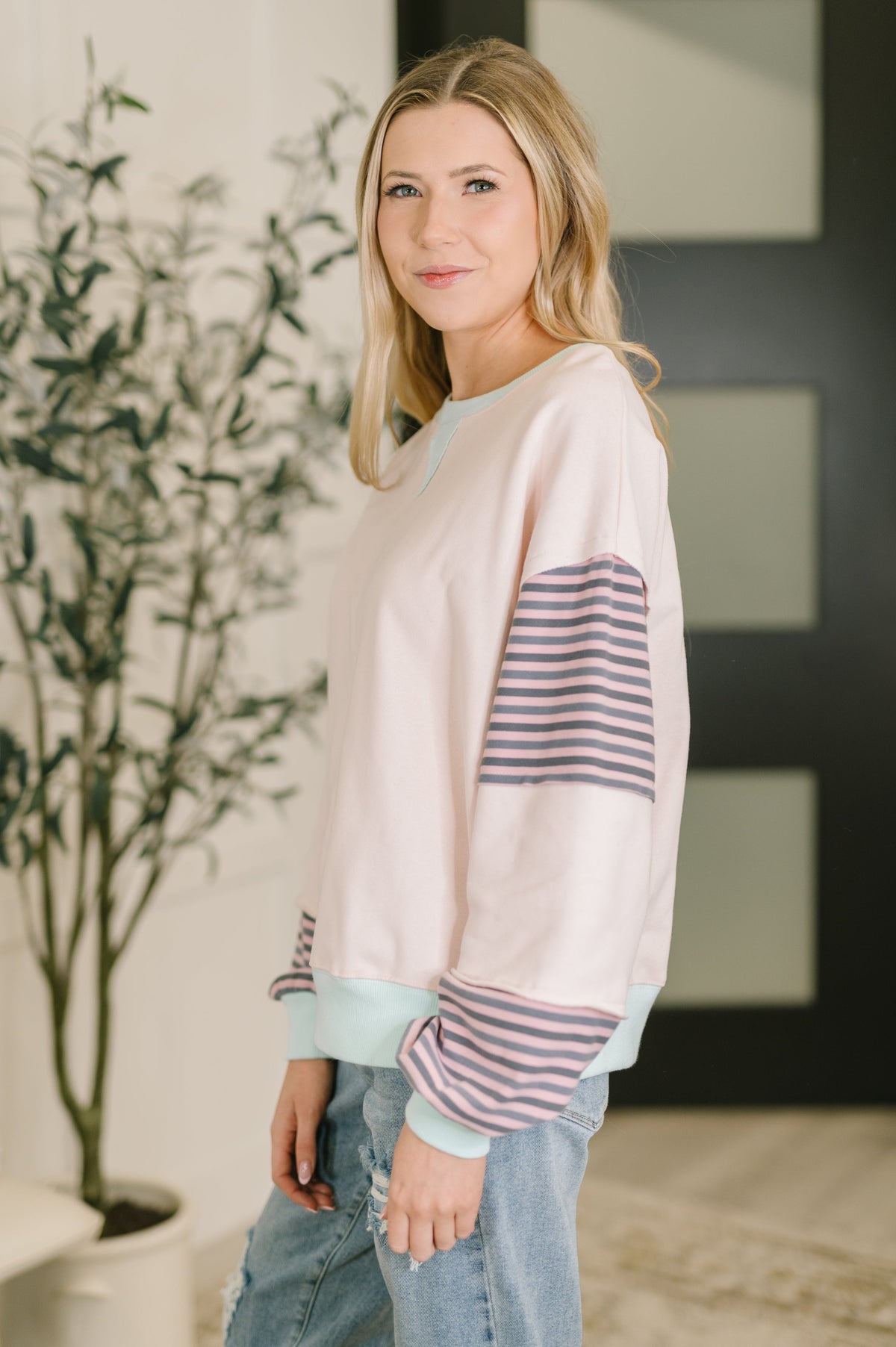 Woman wearing a light pink sweater with striped sleeves in an indoor setting.