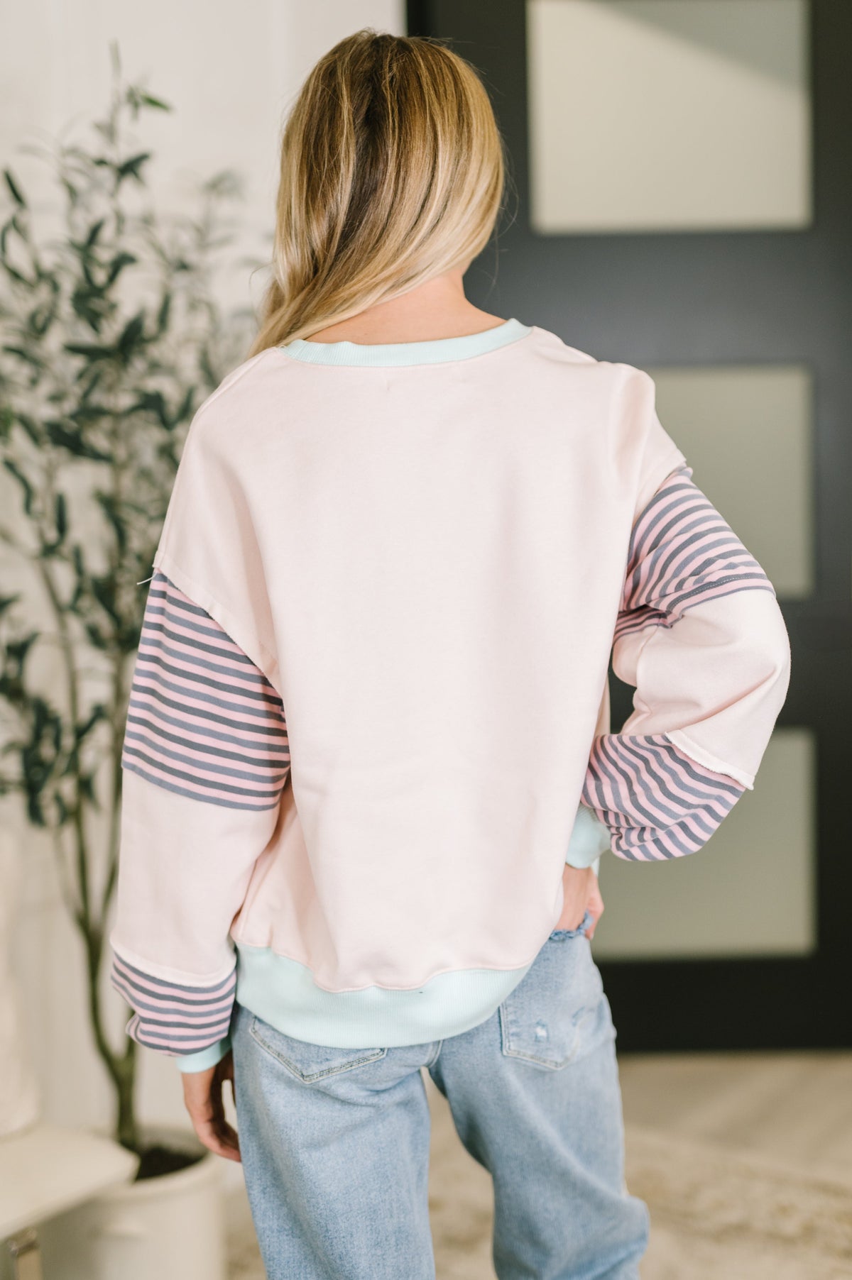 Person wearing a light pink sweater with striped sleeves and blue jeans indoors.