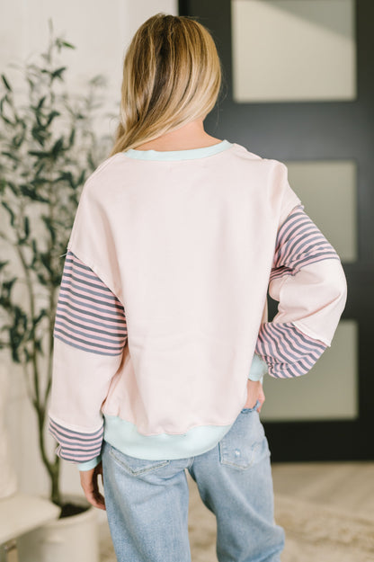 Person wearing a light pink sweater with striped sleeves and blue jeans indoors.