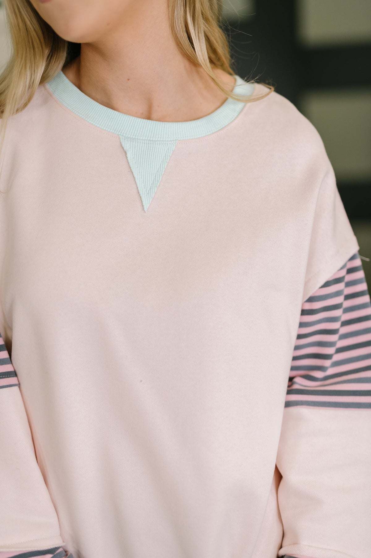 Close-up of a person wearing a light pink sweater with blue and striped sleeves.