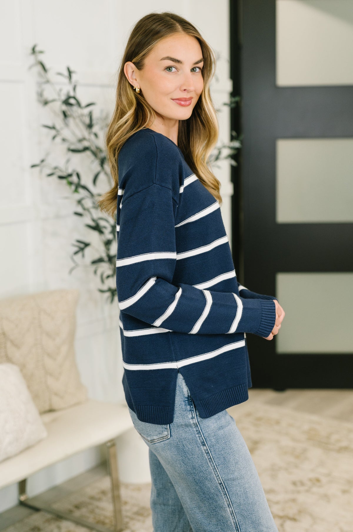 A woman wearing a navy blue and white striped knit sweater with light blue jeans, standing in a bright, modern indoor setting.