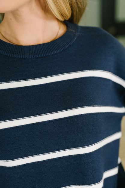 Close-up of a person wearing a navy blue knit sweater with horizontal white stripes.