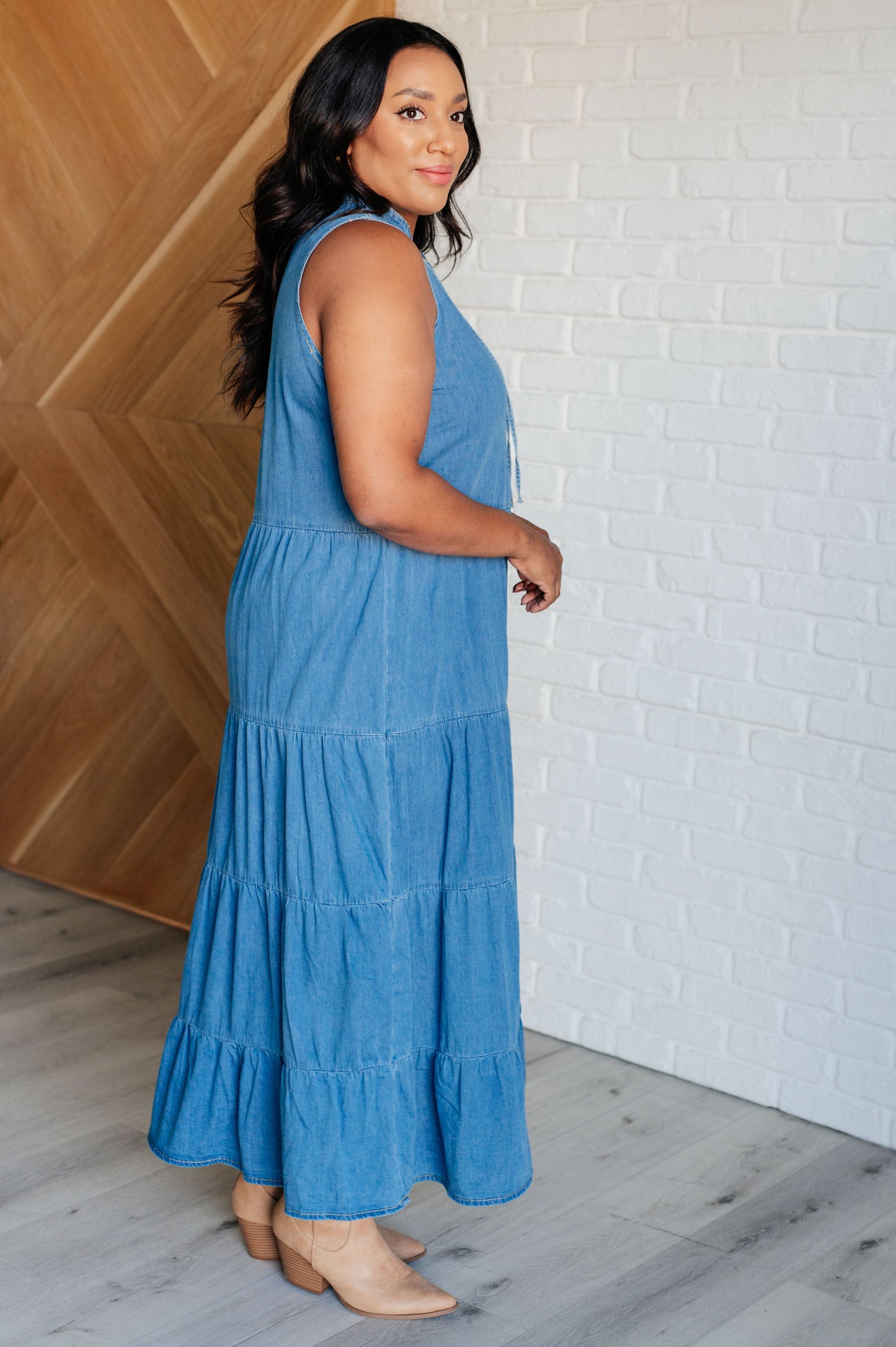 Woman wearing a blue dress standing against a white brick wall.