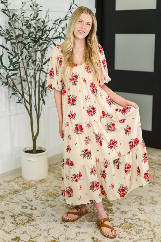 Woman wearing a floral dress standing in a room with a plant and decorative wall.