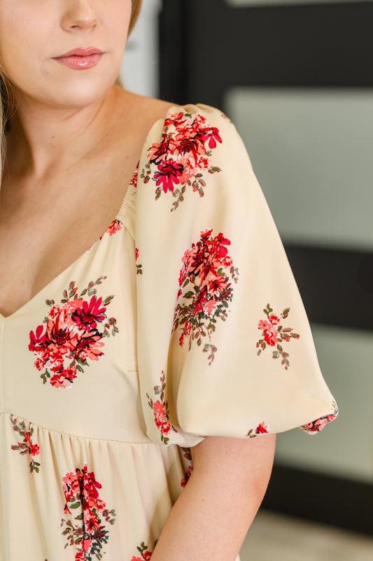 Beige dress with red floral patterns worn by a person, blurred background