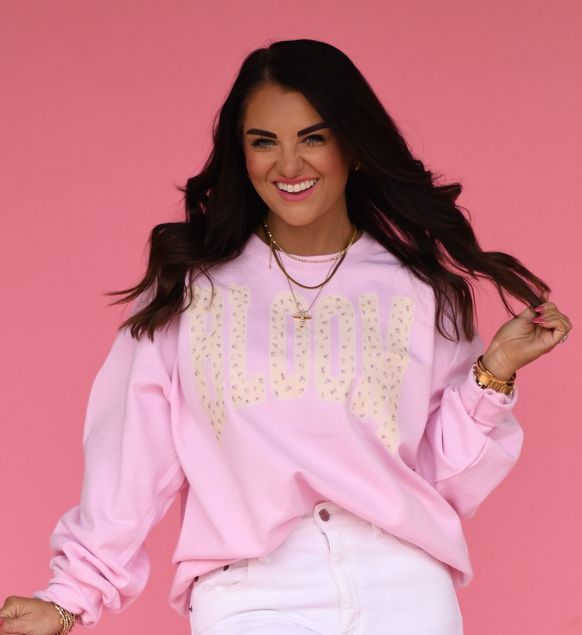 Woman wearing a pink sweatshirt with Bloom Floral text against a pink background