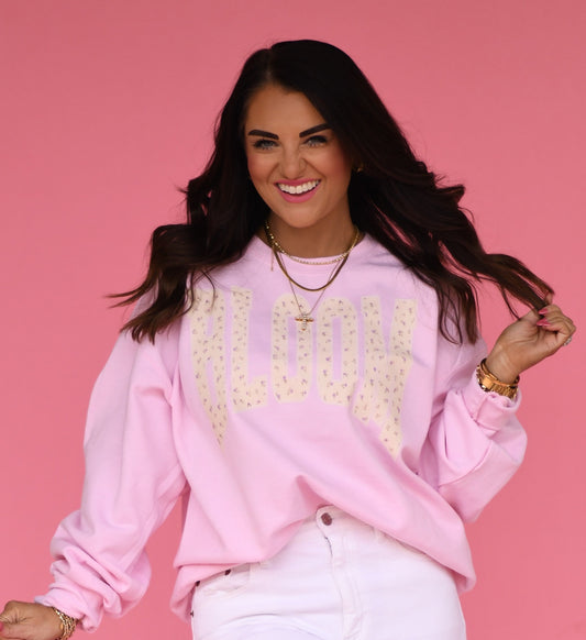 Woman wearing a pink sweatshirt with Bloom Floral text against a pink background
