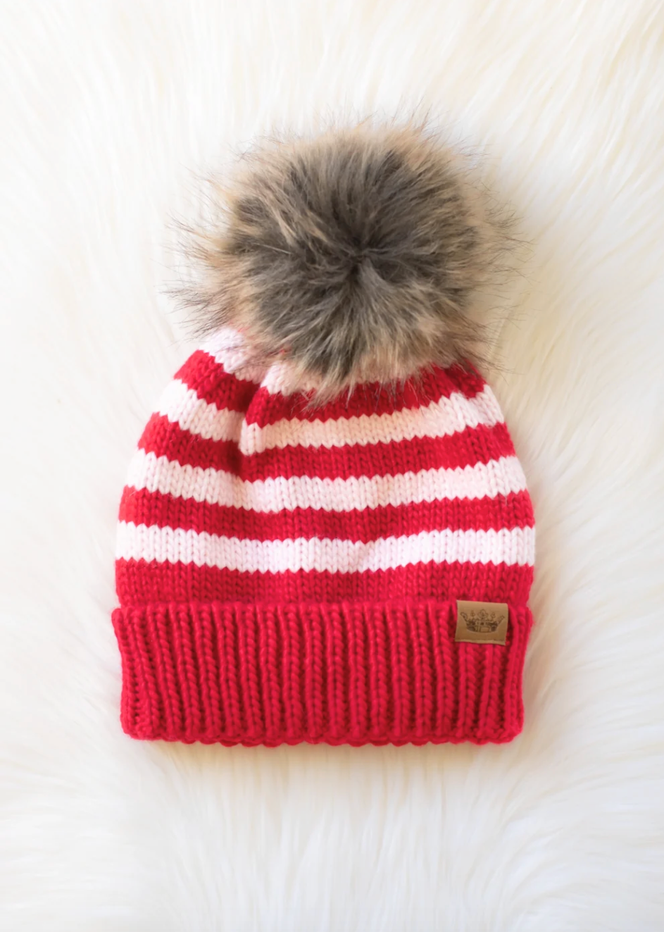 Red and white striped knit hat with a fur pom-pom on a white background