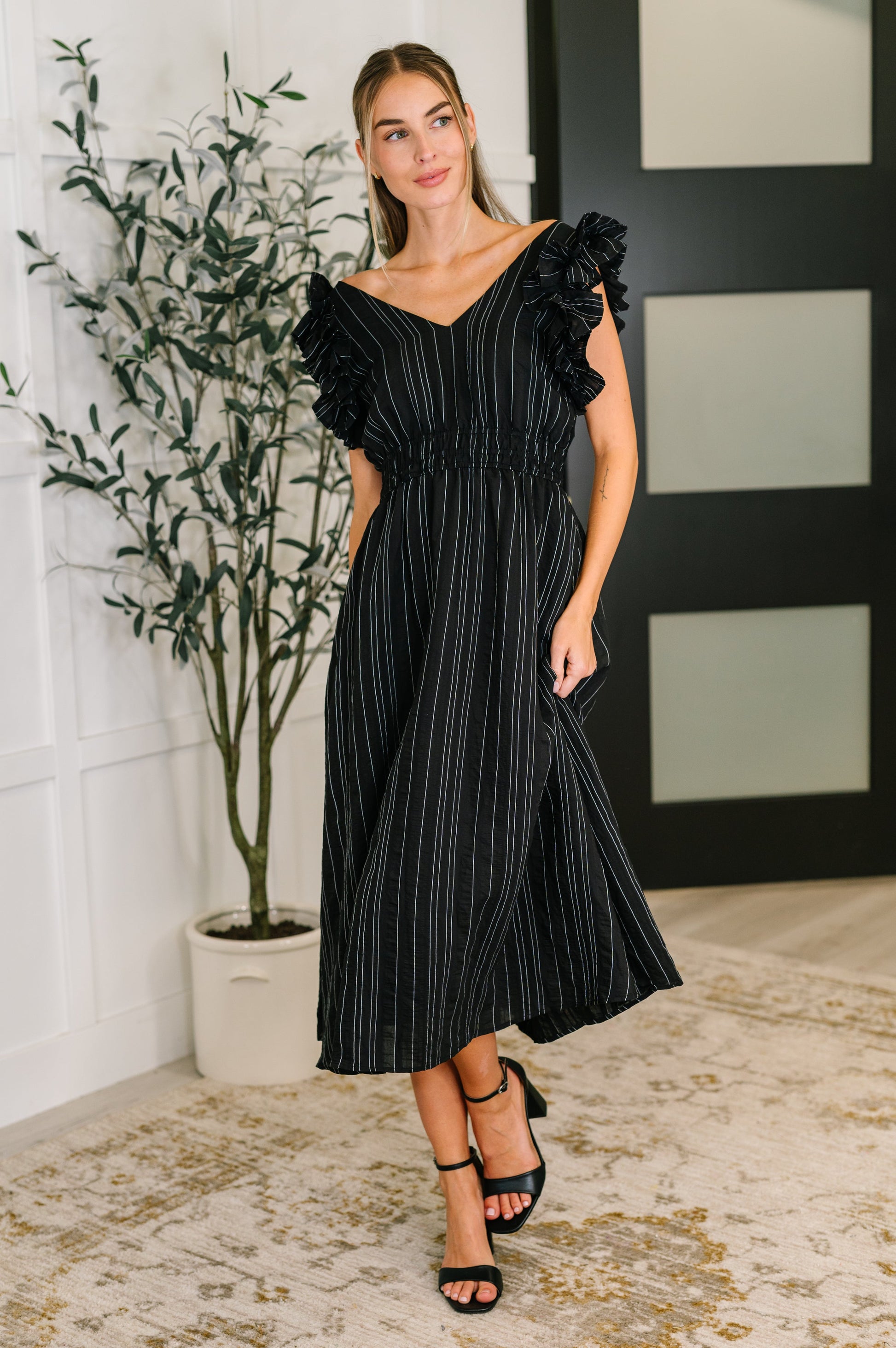 Woman wearing a black striped dress with ruffled shoulders in an indoor setting.