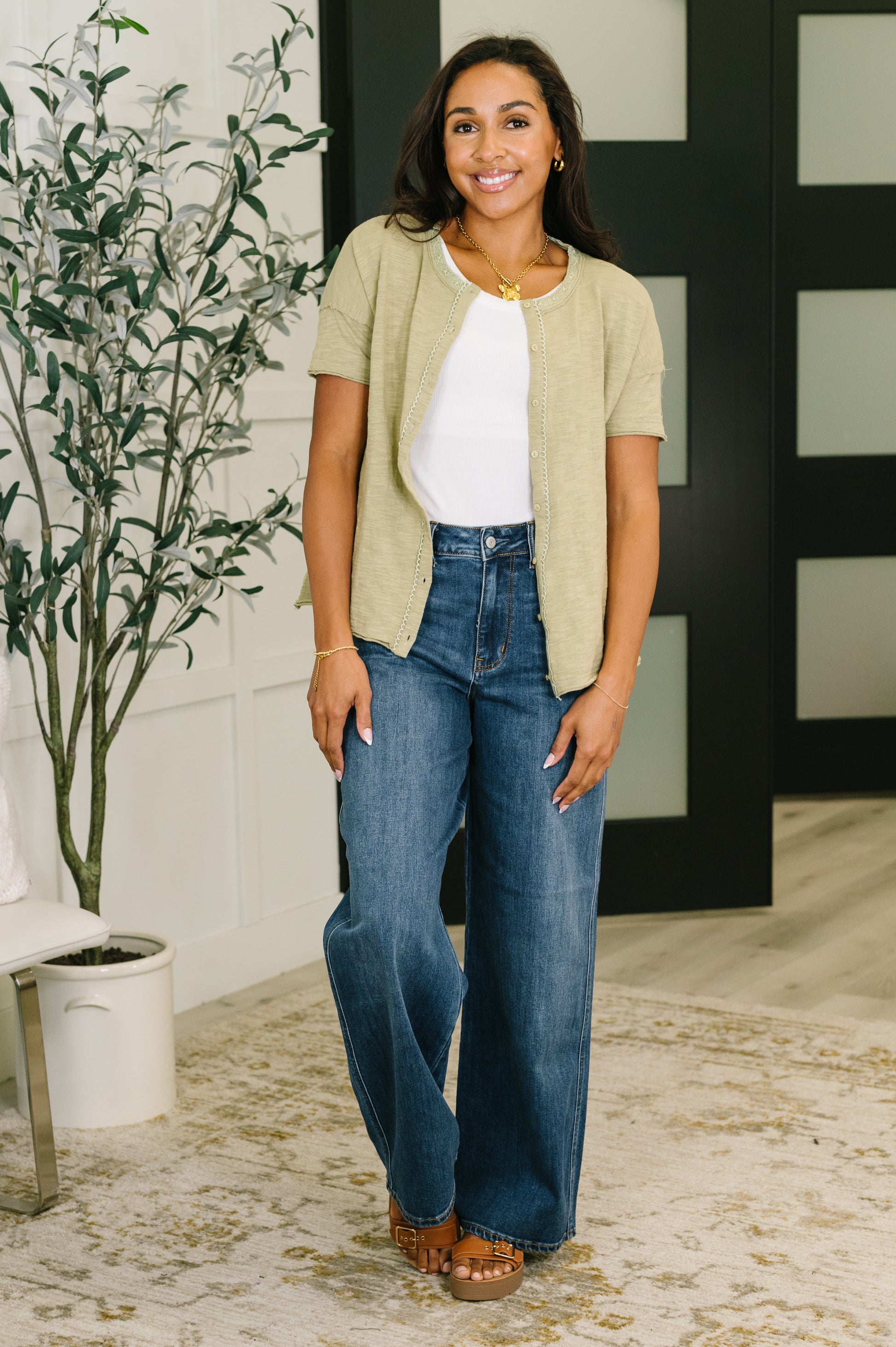 Woman wearing a beige cardigan, white shirt, and blue jeans indoors.